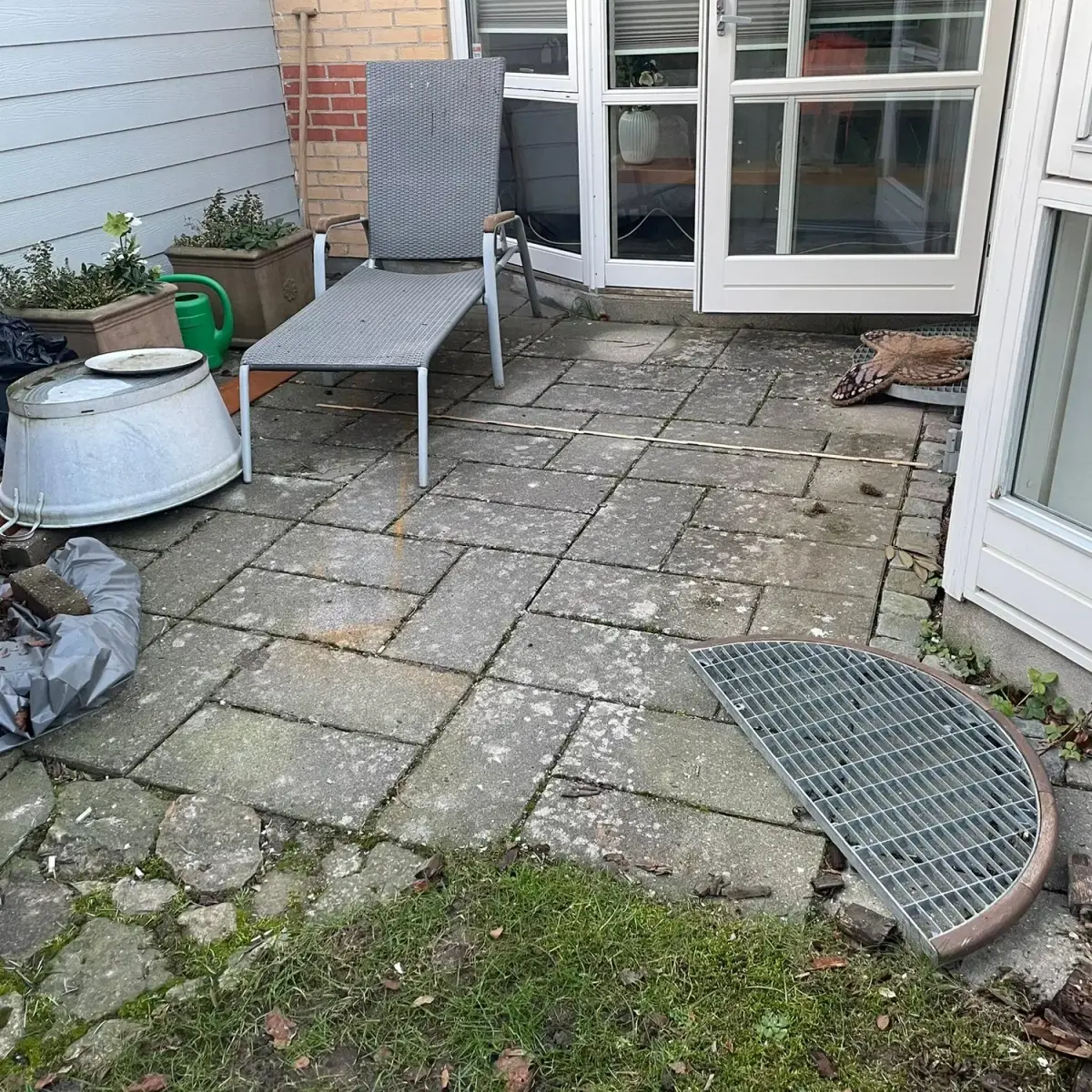 Ældre terrasse i slidte, mosgroede betonfliser helt inde ved huset